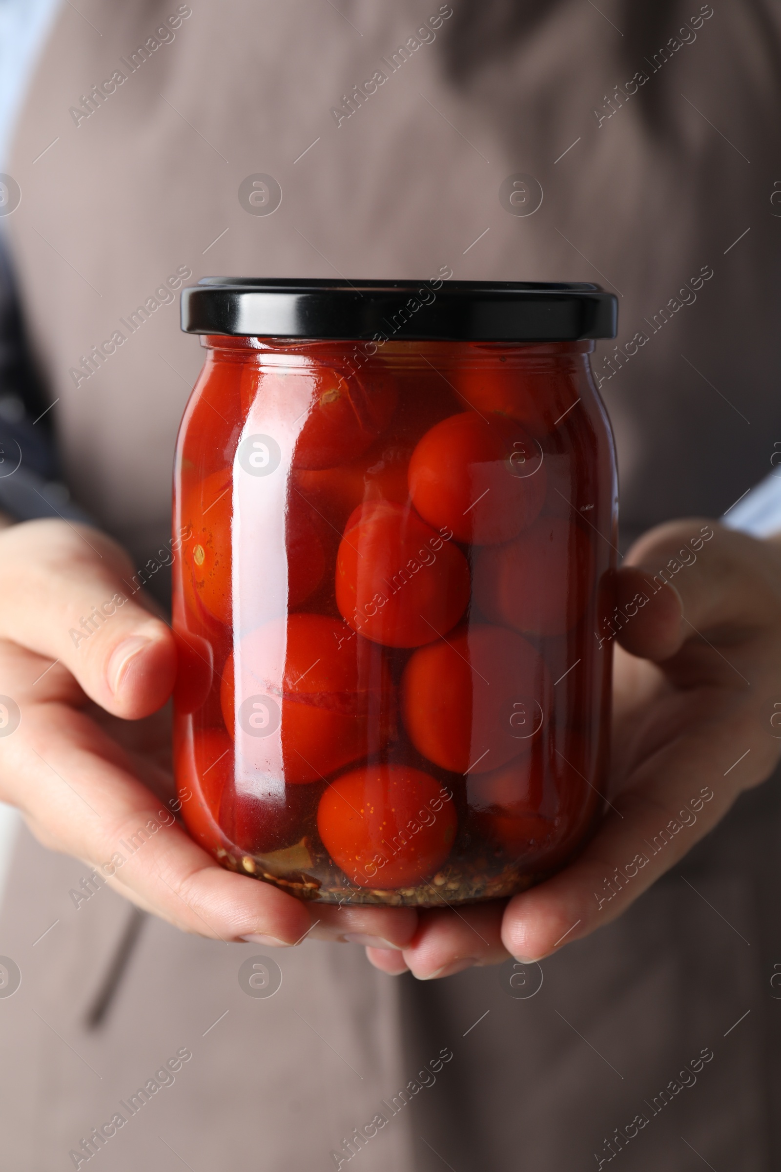 Photo of Woman holding jar with tasty pickled tomatoes, closeup