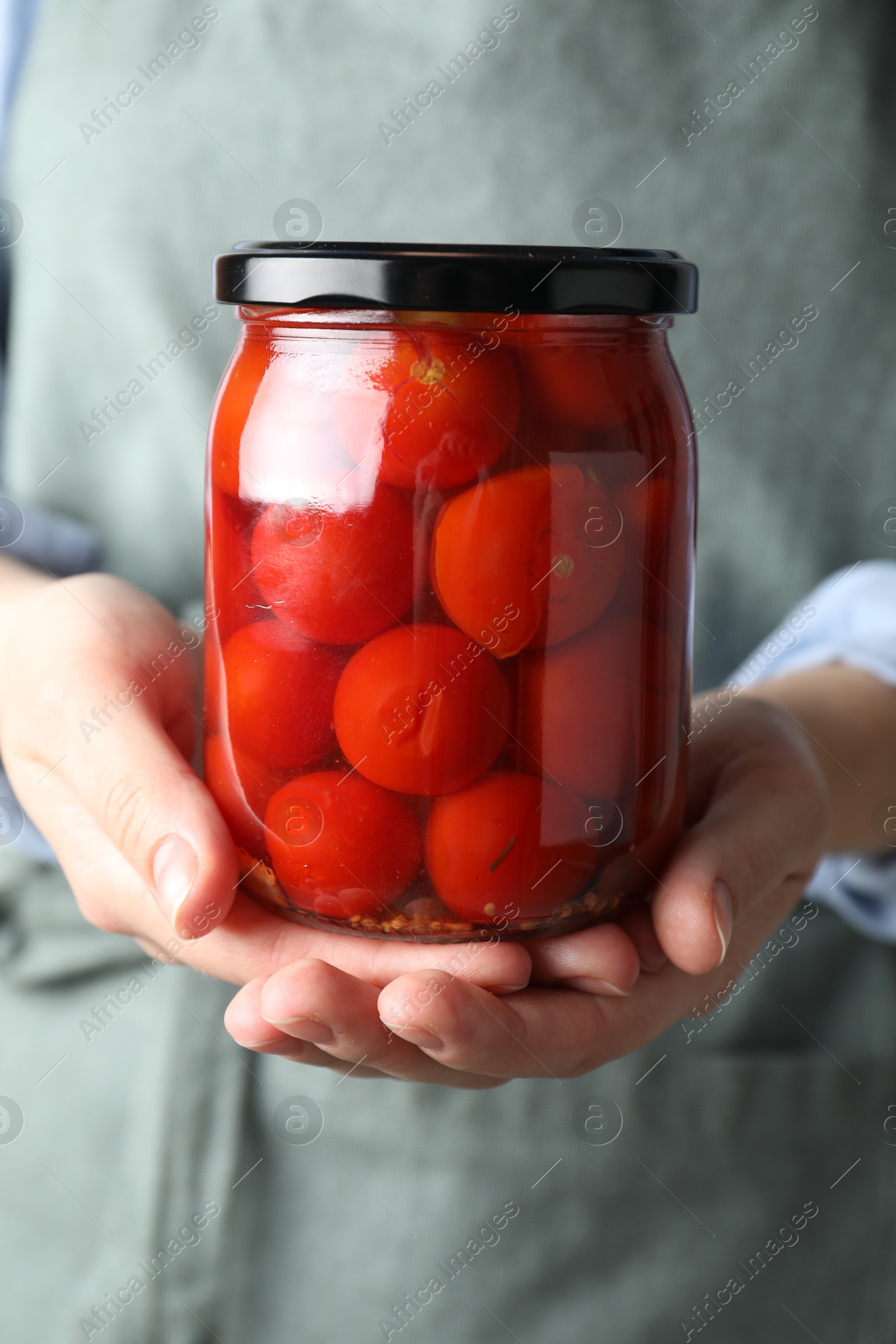 Photo of Woman holding jar with tasty pickled tomatoes, closeup