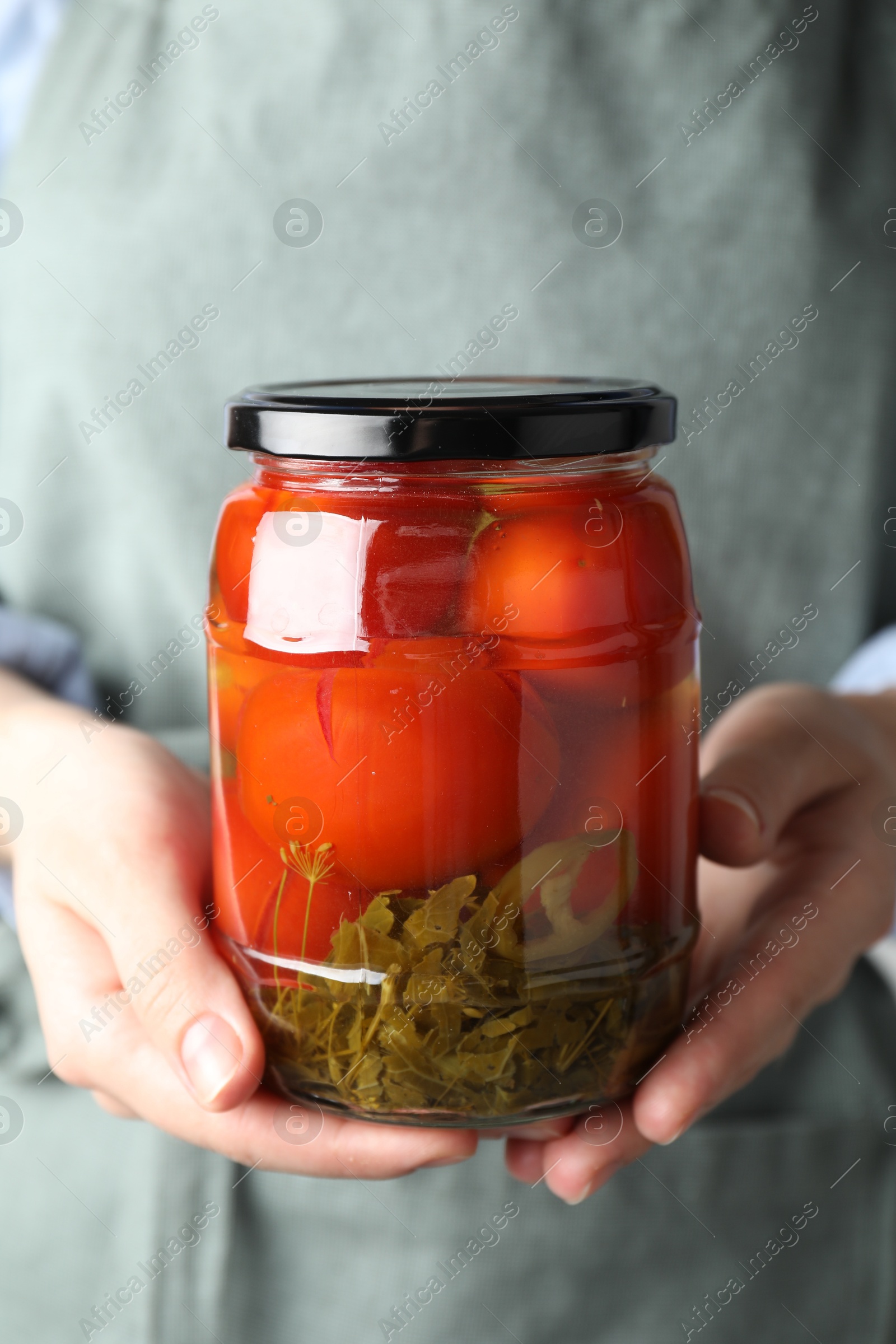 Photo of Woman holding jar with tasty pickled tomatoes, closeup