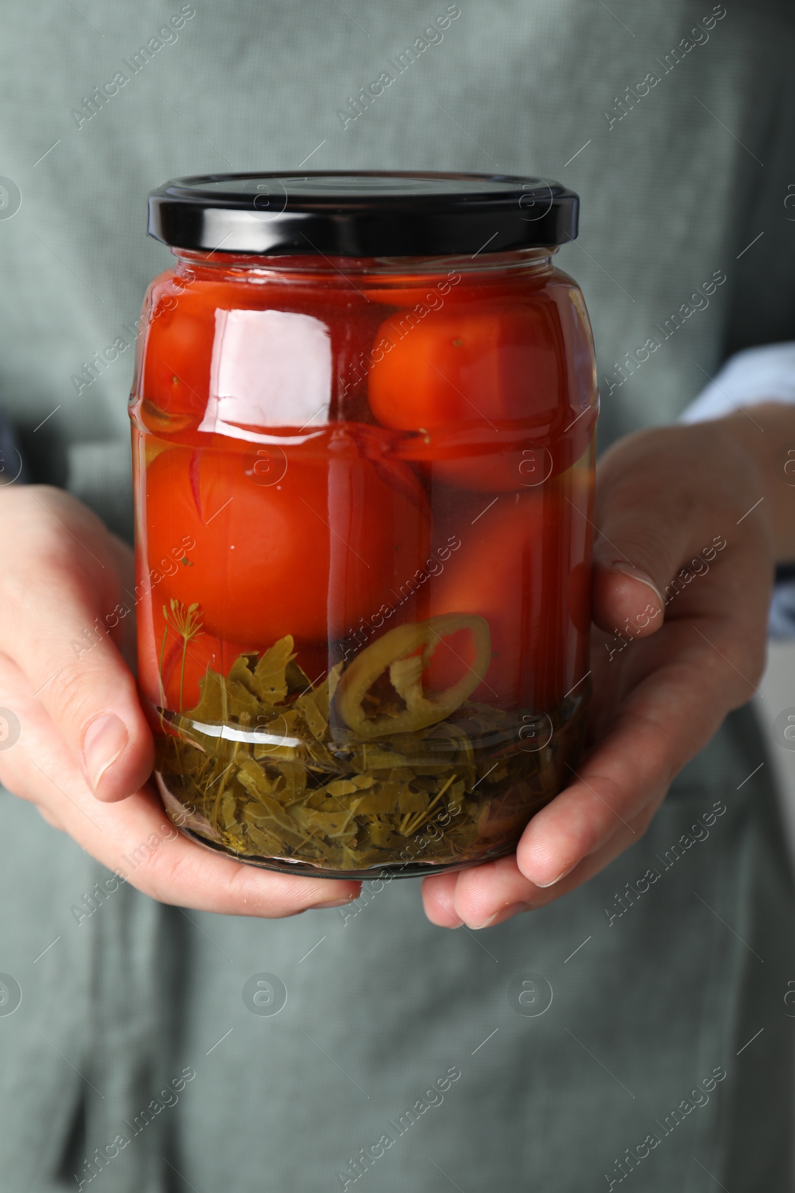 Photo of Woman holding jar with tasty pickled tomatoes, closeup