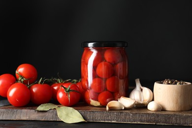 Tasty pickled tomatoes in jar, spices and fresh vegetables on wooden table