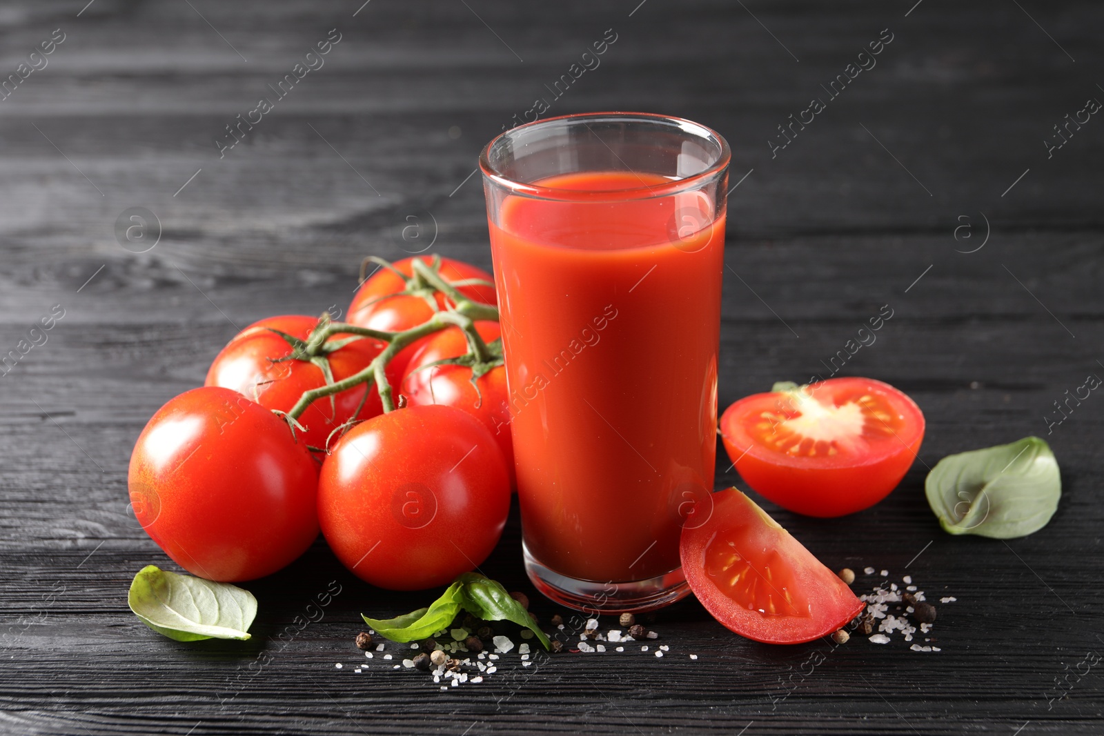 Photo of Tasty tomato juice in glass with fresh vegetables and spices on black wooden table