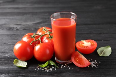 Tasty tomato juice in glass with fresh vegetables and spices on black wooden table