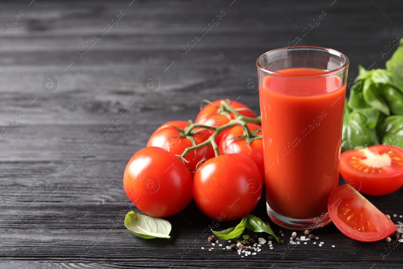 Photo of Tasty tomato juice in glass with fresh vegetables and spices on black wooden table. Space for text