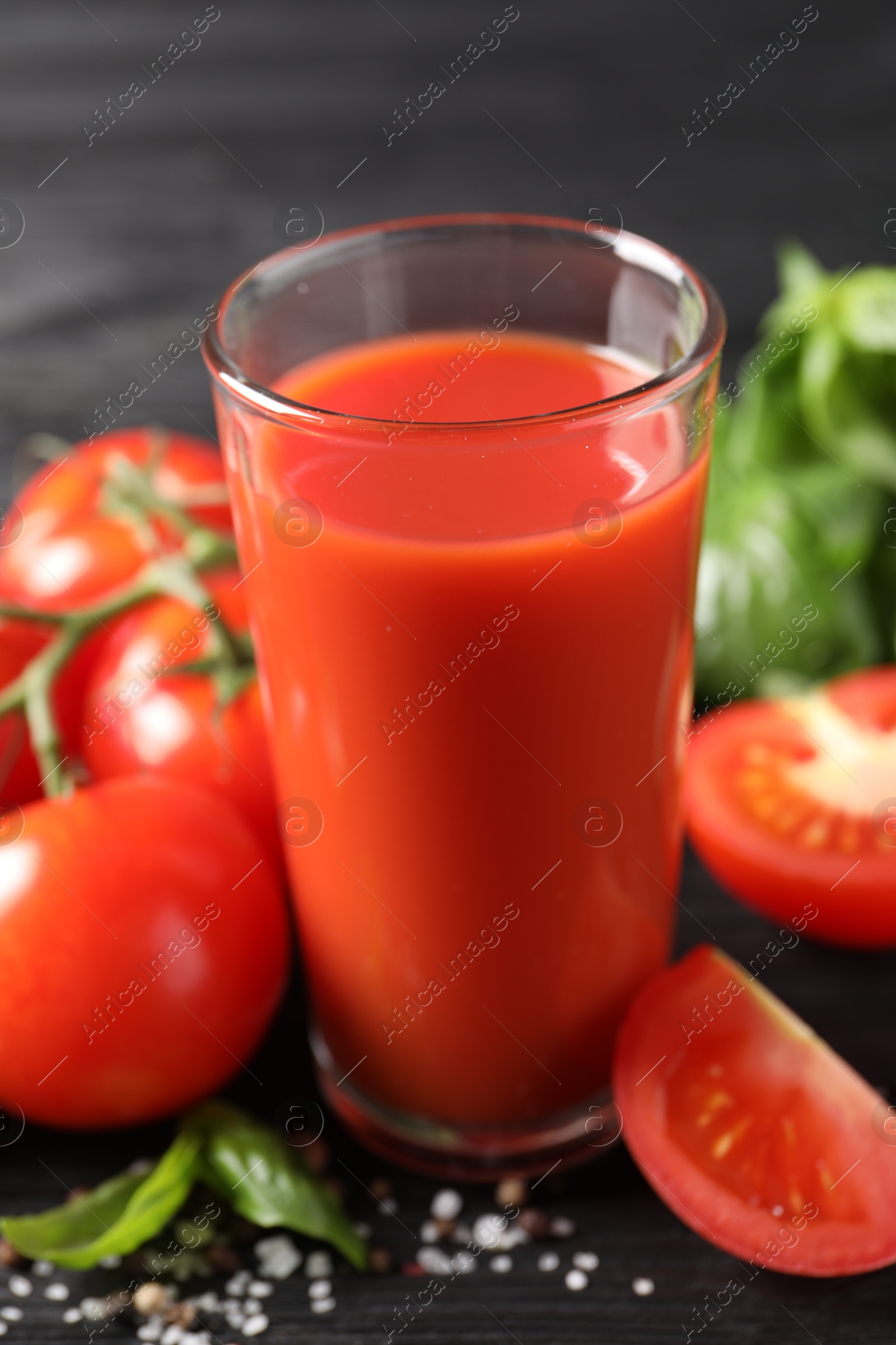 Photo of Tasty tomato juice in glass with fresh vegetables and spices on black table, closeup