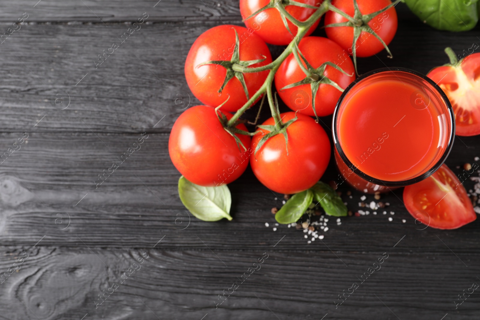 Photo of Tasty tomato juice in glass with fresh vegetables and spices on black wooden table, flat lay. Space for text