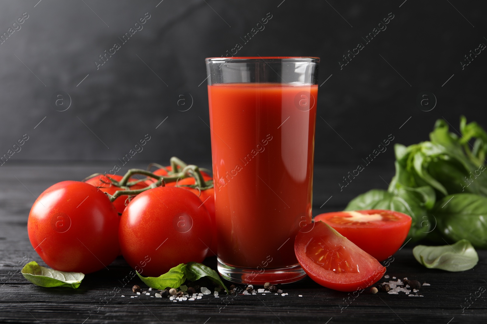 Photo of Tasty tomato juice in glass with fresh vegetables and spices on black wooden table