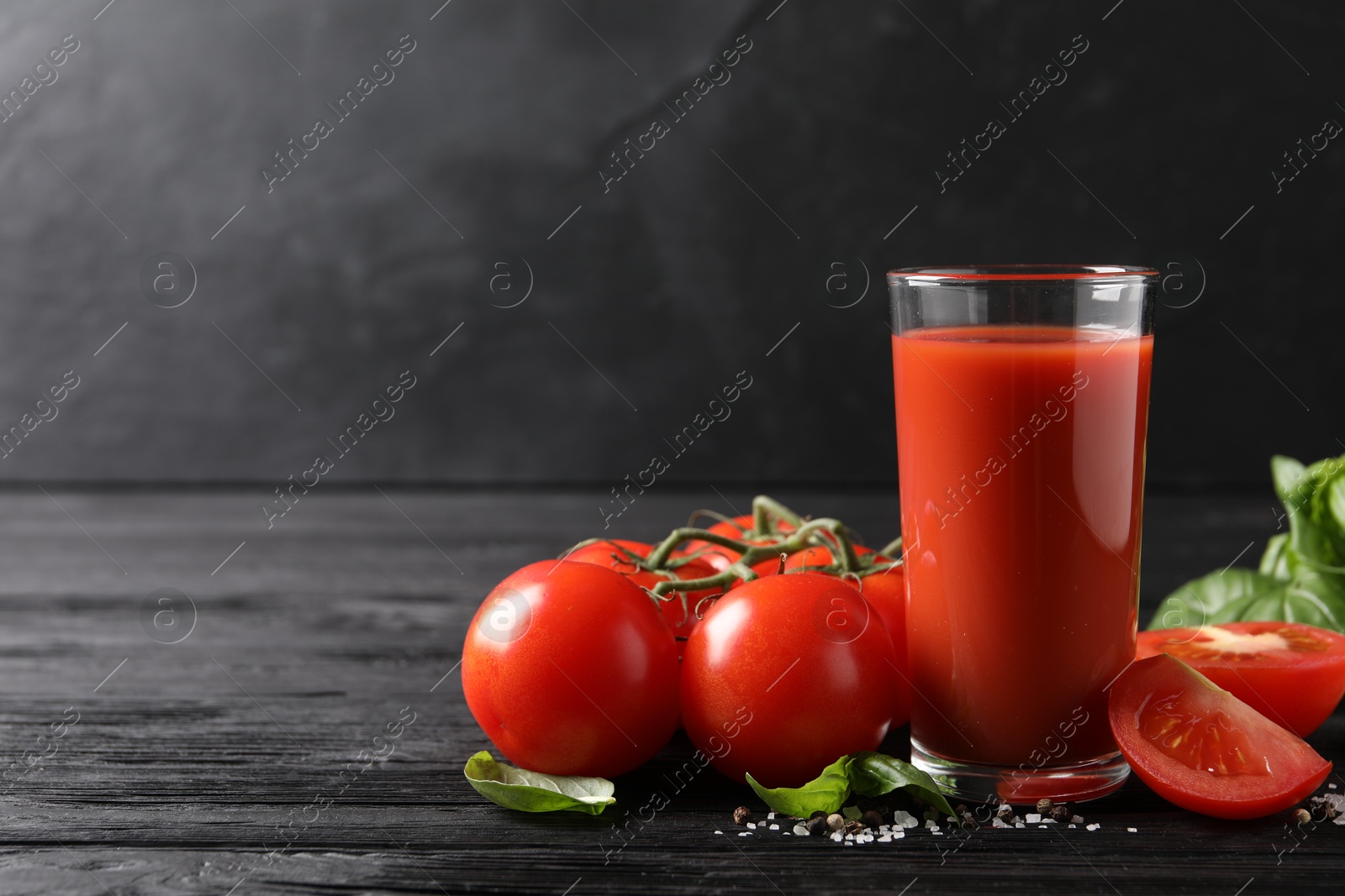 Photo of Tasty tomato juice in glass with fresh vegetables and spices on black wooden table. Space for text