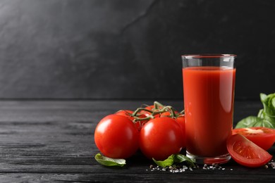 Tasty tomato juice in glass with fresh vegetables and spices on black wooden table. Space for text