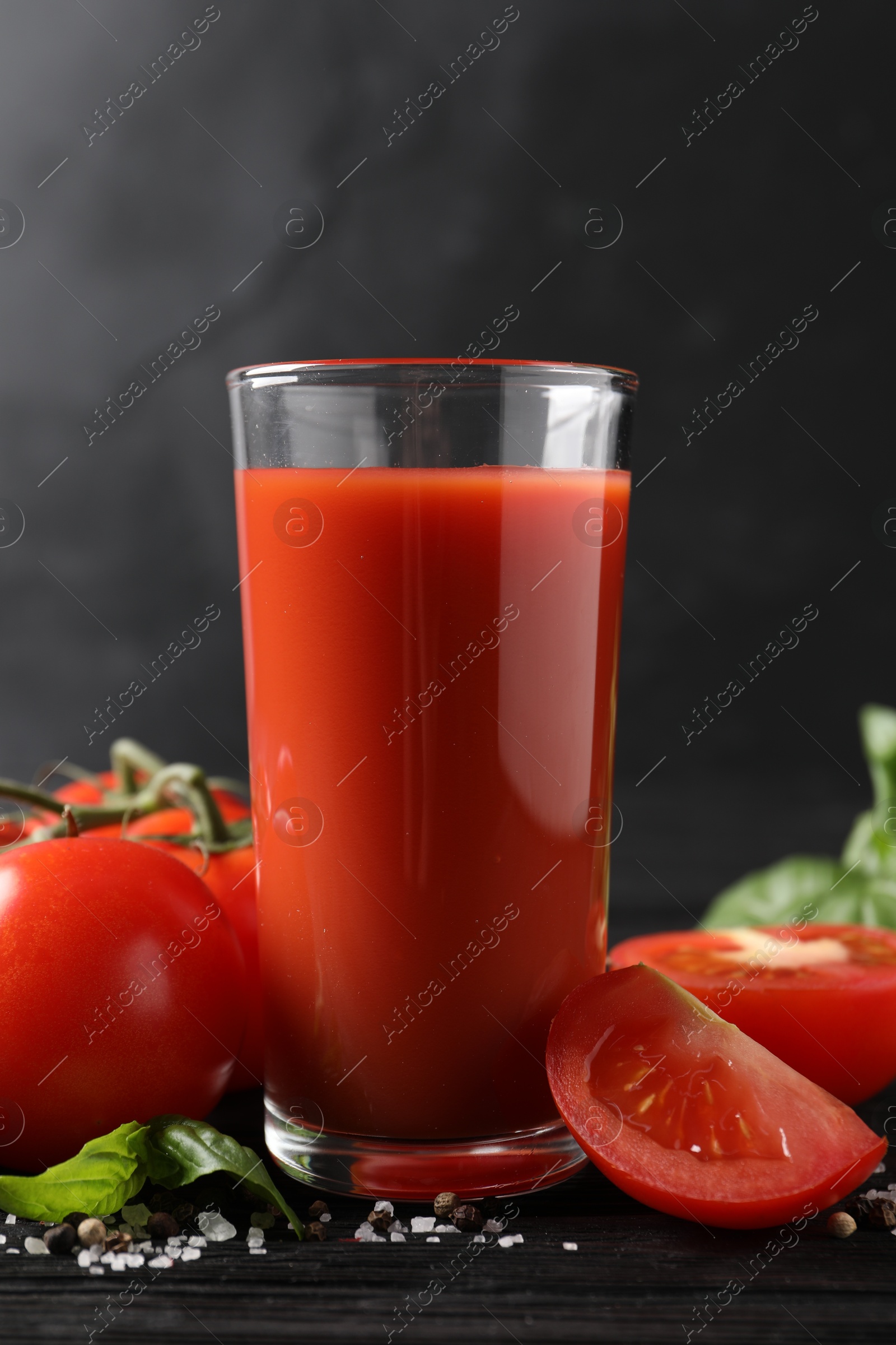 Photo of Tasty tomato juice in glass with fresh vegetables and spices on black wooden table, closeup