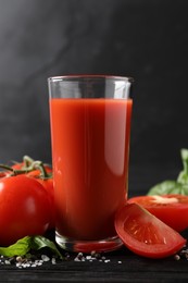 Tasty tomato juice in glass with fresh vegetables and spices on black wooden table, closeup