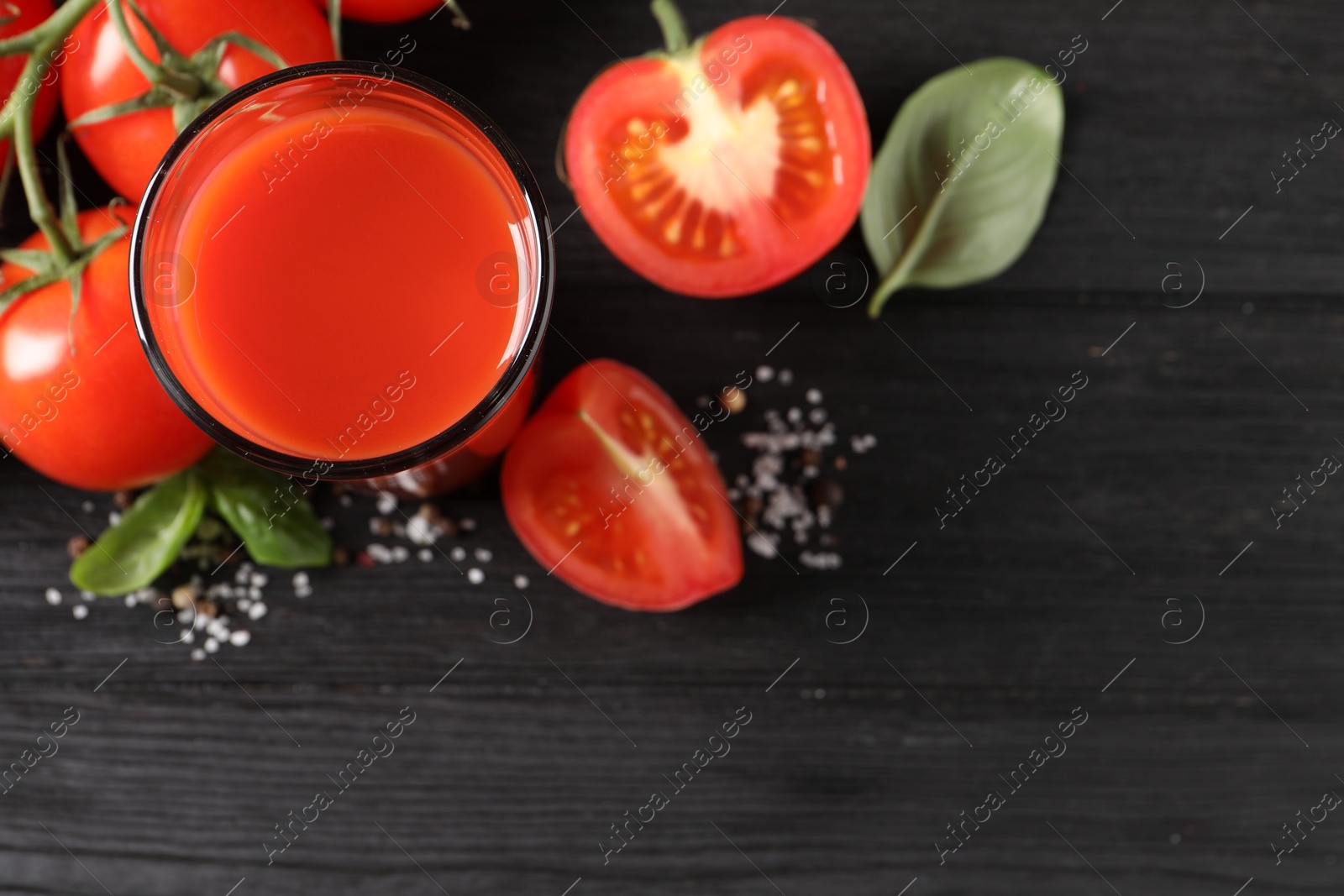 Photo of Tasty tomato juice in glass with fresh vegetables and spices on black wooden table, flat lay. Space for text