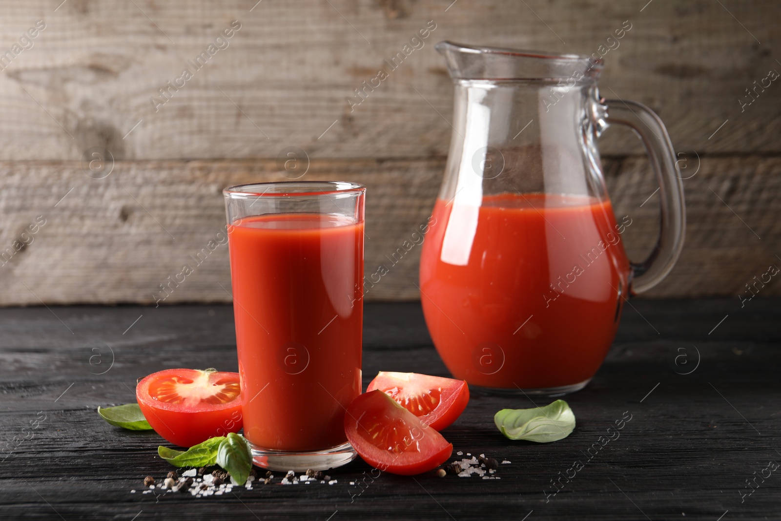 Photo of Tasty tomato juice with fresh vegetables and spices on black wooden table