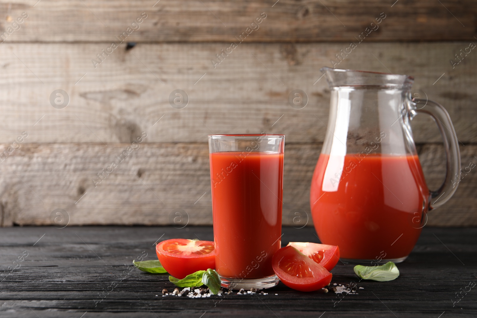 Photo of Tasty tomato juice with fresh vegetables and spices on black wooden table, space for text