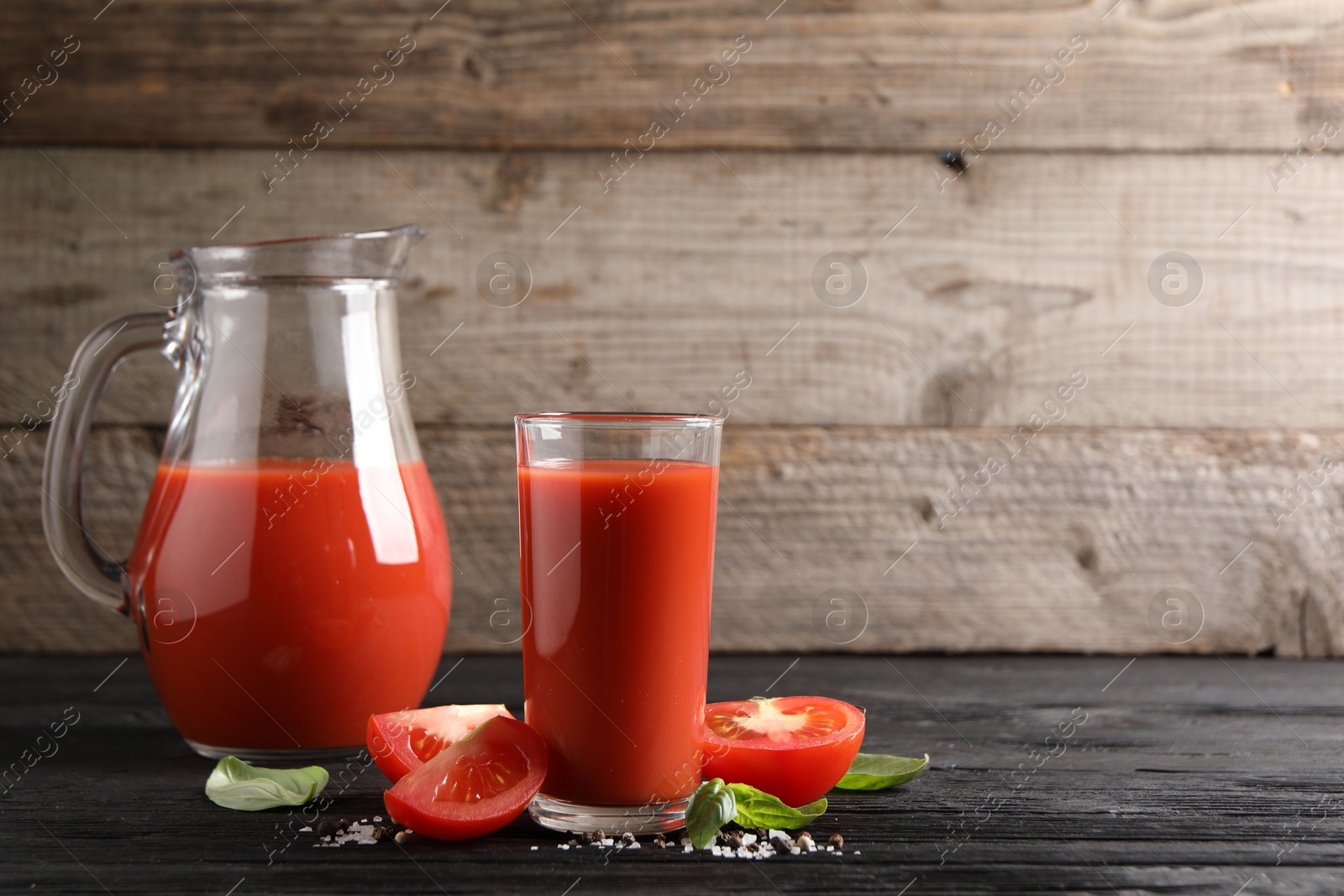 Photo of Tasty tomato juice with fresh vegetables and spices on black wooden table, space for text