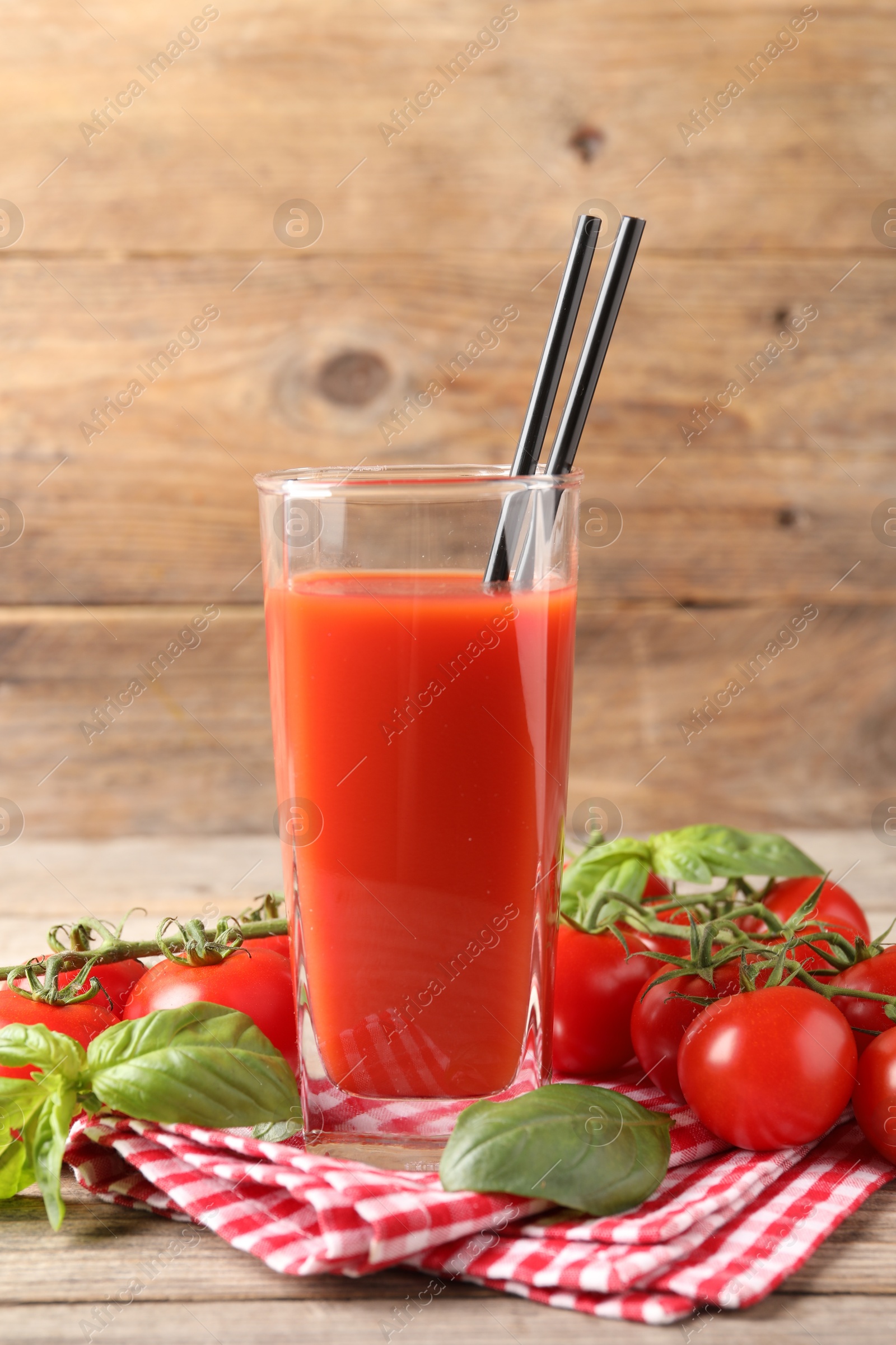 Photo of Tasty tomato juice in glass with basil leaves and fresh vegetables on wooden table