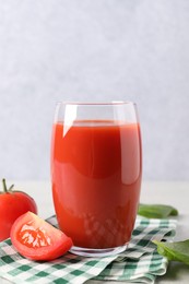 Tasty tomato juice in glass, basil leaves and fresh vegetables on light table