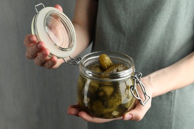 Woman opening jar with pickled cucumbers on grey background, closeup