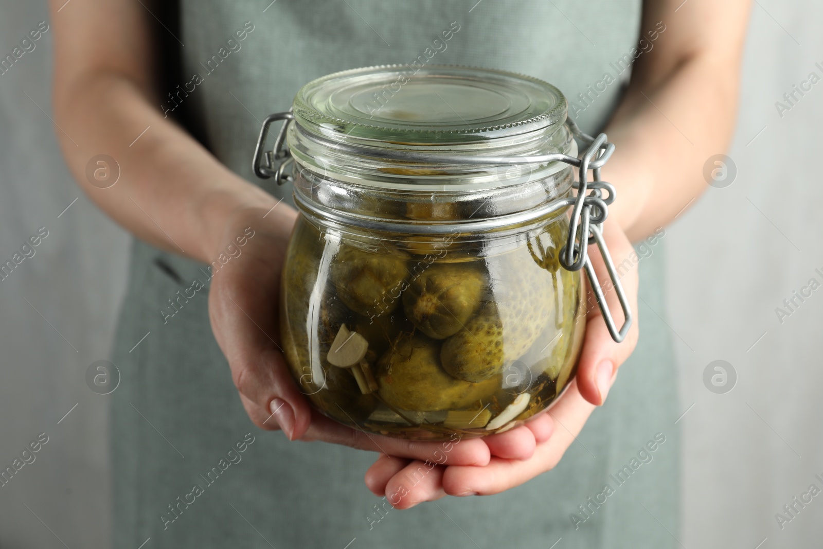 Photo of Woman holding jar with pickled cucumbers on grey background, closeup