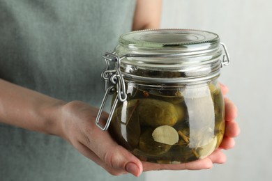 Woman holding jar with pickled cucumbers on grey background, closeup