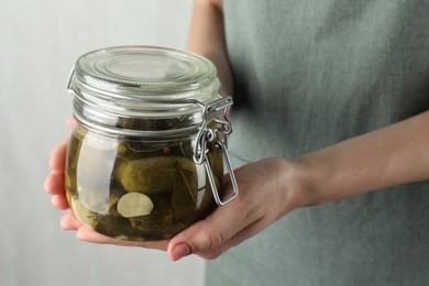 Photo of Woman holding jar with pickled cucumbers on grey background, closeup