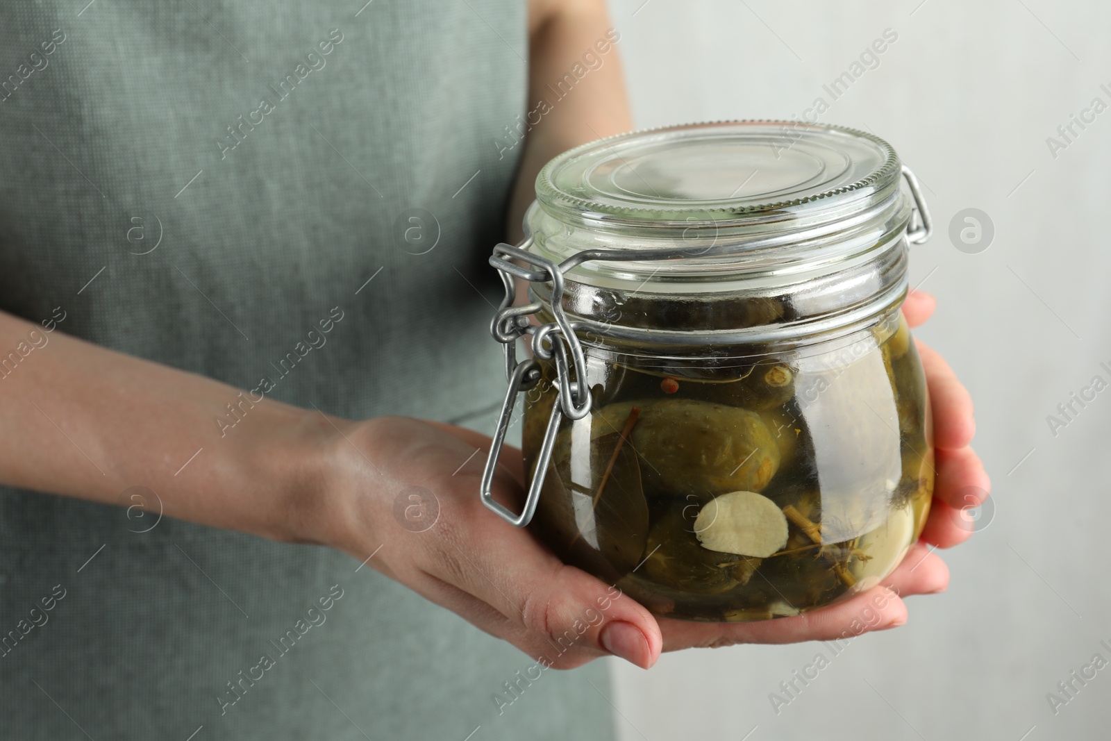 Photo of Woman holding jar with pickled cucumbers on grey background, closeup