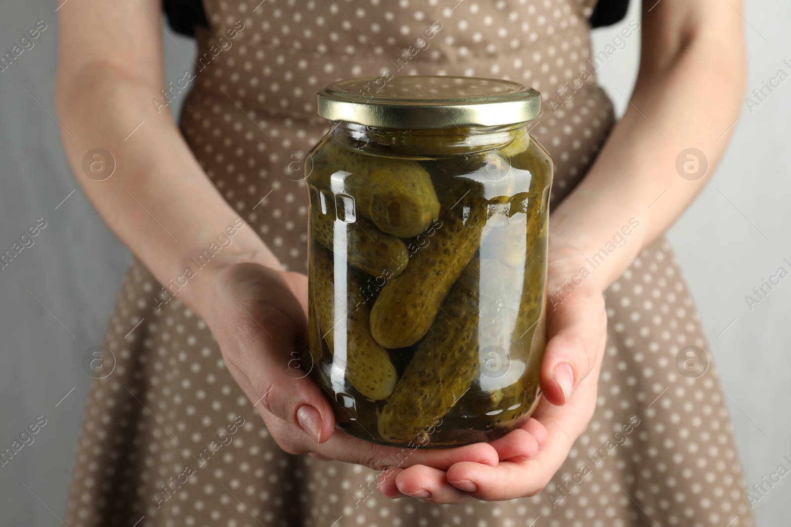 Photo of Woman holding jar with pickled cucumbers on grey background, closeup