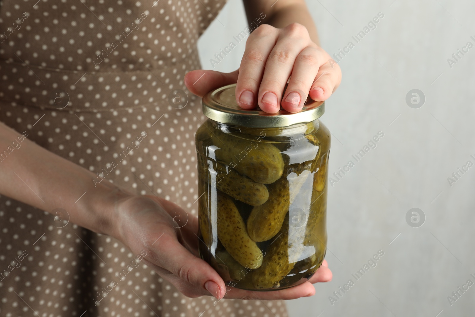 Photo of Woman holding jar with pickled cucumbers on grey background, closeup