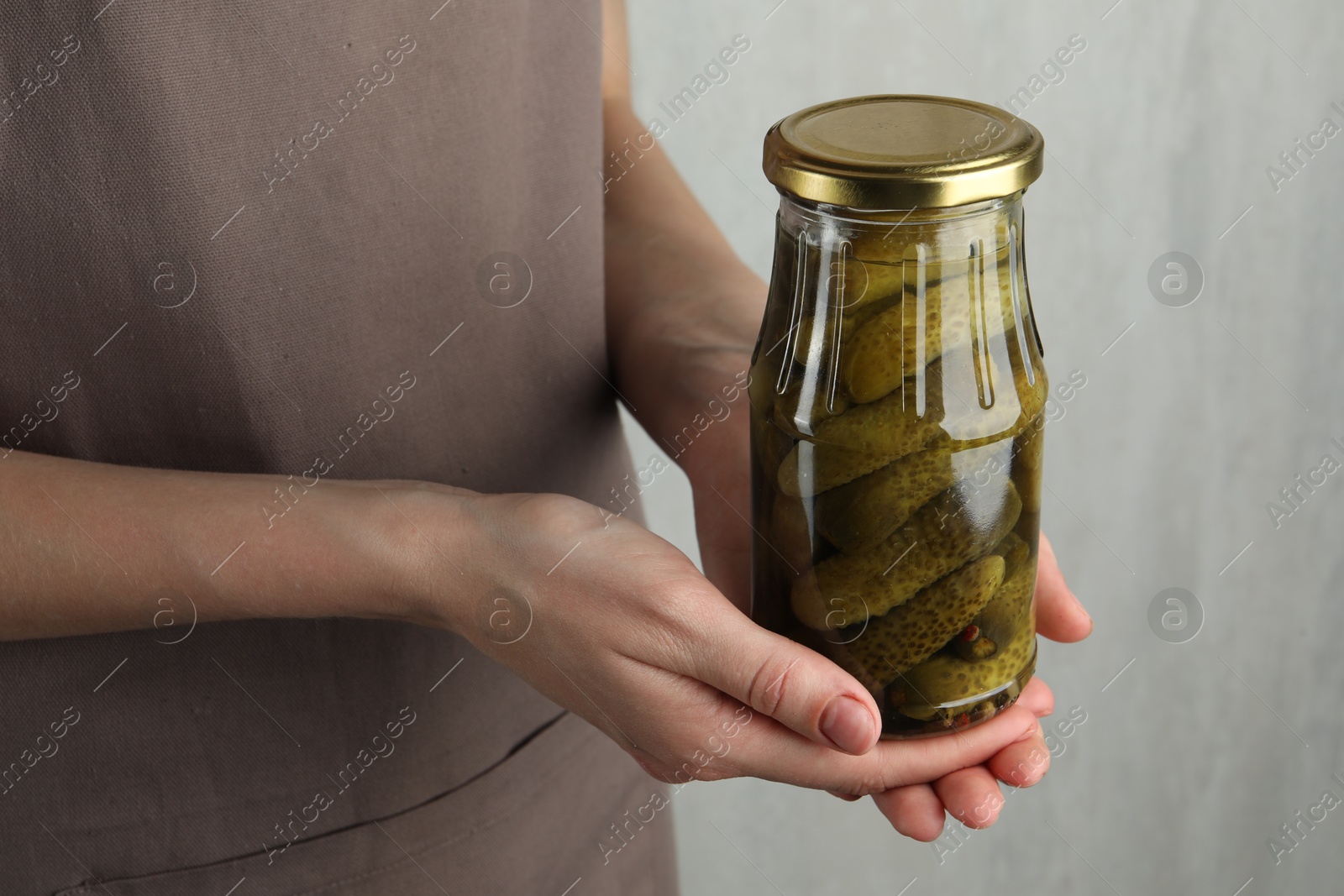 Photo of Woman holding jar with pickled cucumbers on grey background, closeup