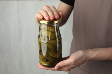 Photo of Woman holding jar with pickled cucumbers on grey background, closeup. Space for text