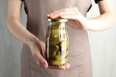 Photo of Woman holding jar with pickled cucumbers on grey background, closeup