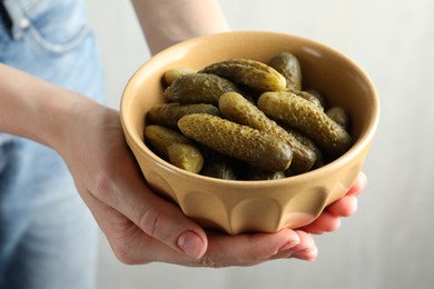 Photo of Woman holding bowl with pickled cucumbers on light grey background, closeup