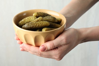 Woman holding bowl with pickled cucumbers on light grey background, closeup