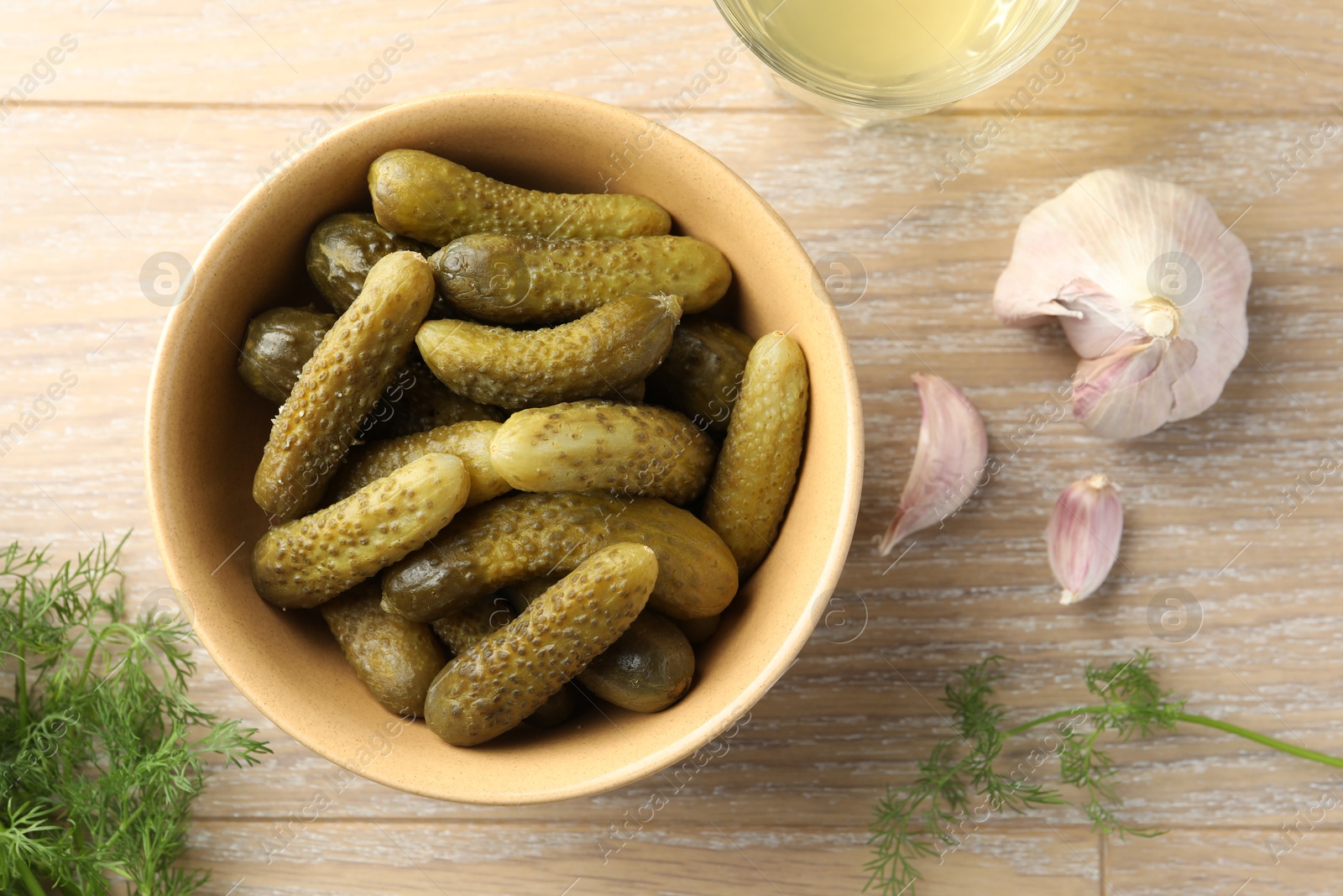 Photo of Pickled cucumbers in bowl, dill, garlic and brine on wooden table, flat lay