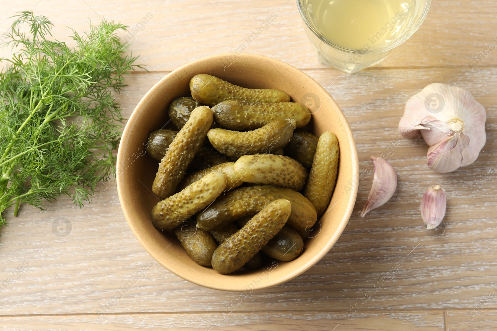 Photo of Pickled cucumbers in bowl, dill, garlic and brine on wooden table, flat lay