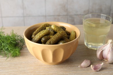 Photo of Pickled cucumbers in bowl, dill, garlic and brine on wooden table, closeup