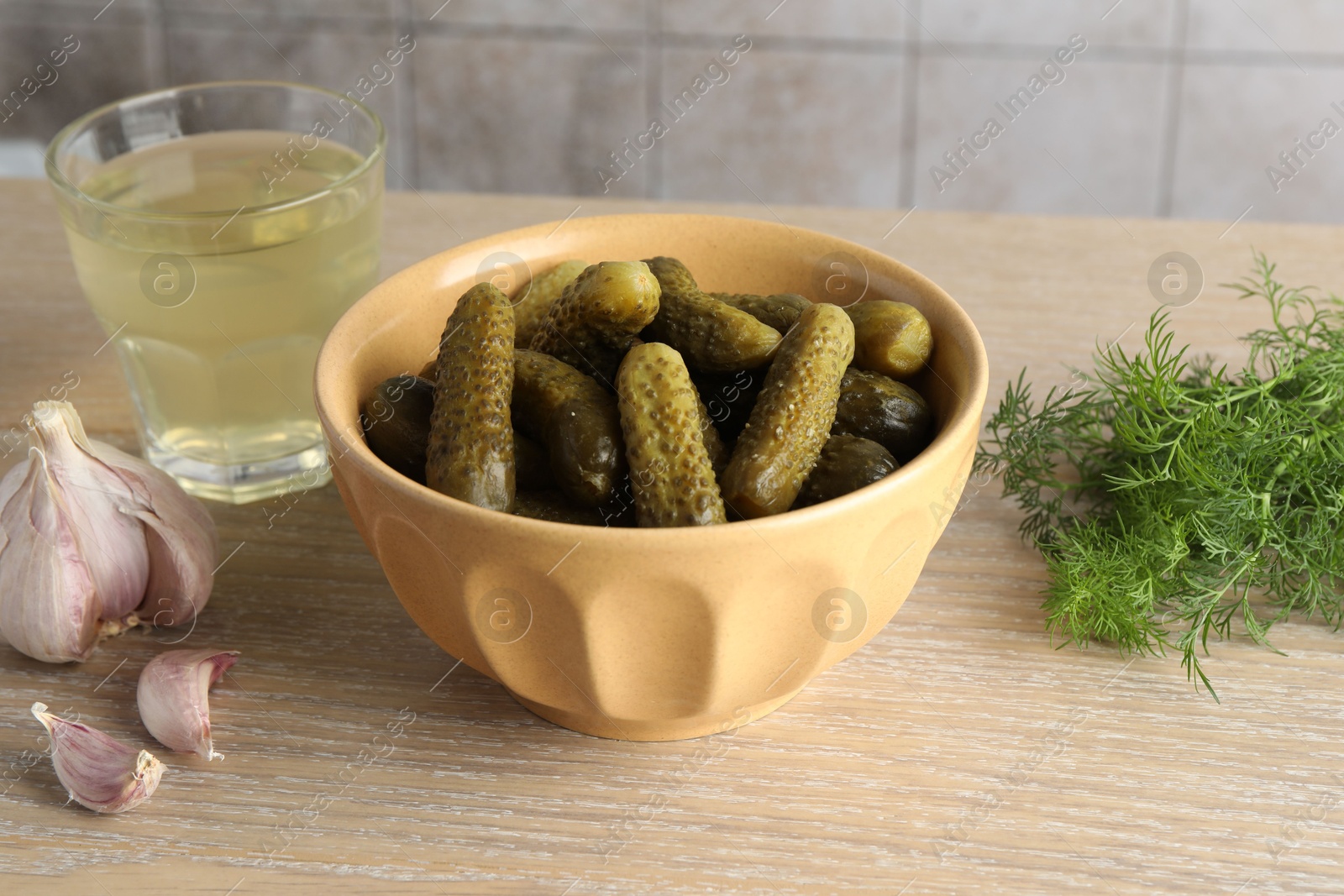 Photo of Pickled cucumbers in bowl, dill, garlic and brine on wooden table, closeup