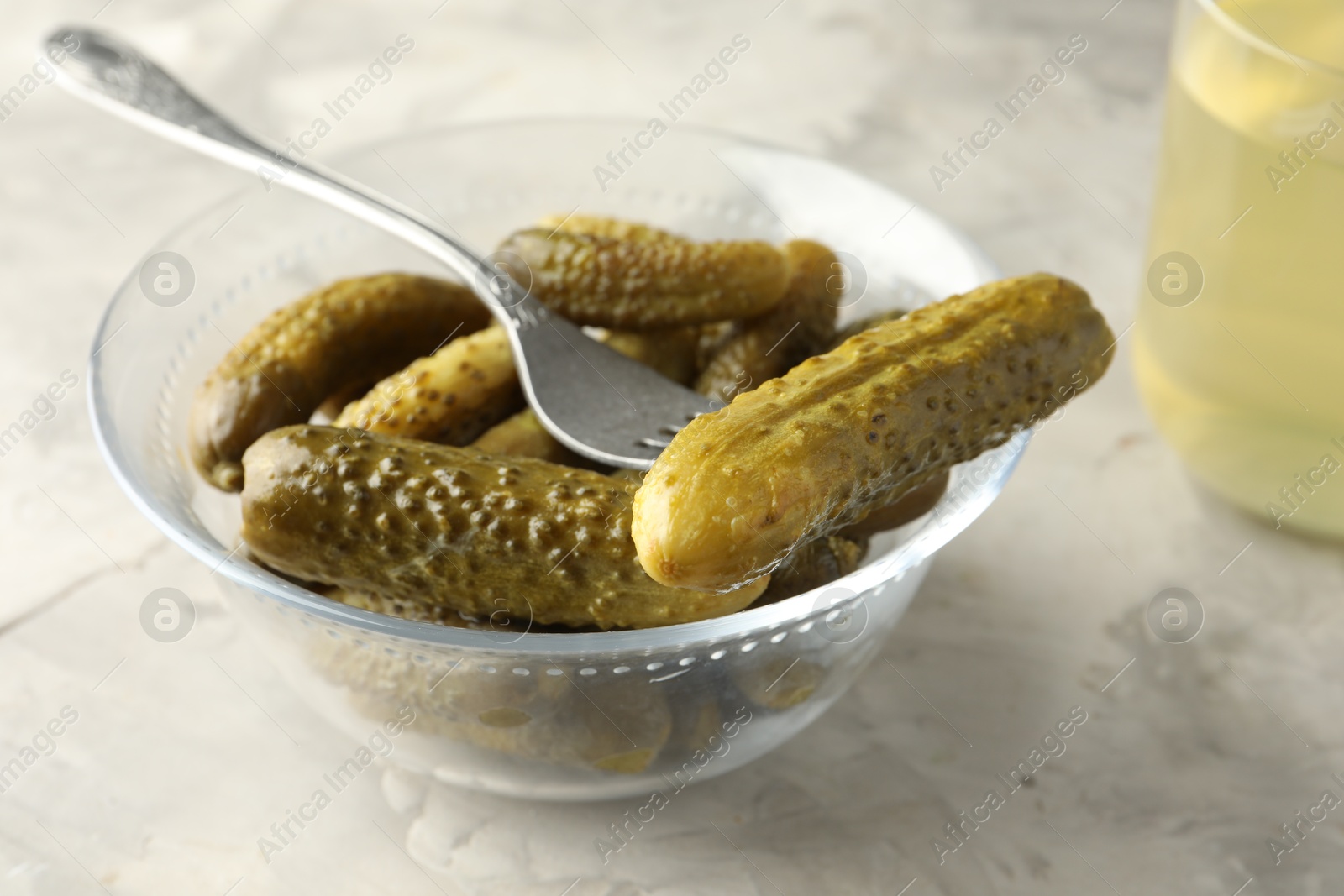 Photo of Pickled cucumbers in bowl and fork on grey textured table, closeup