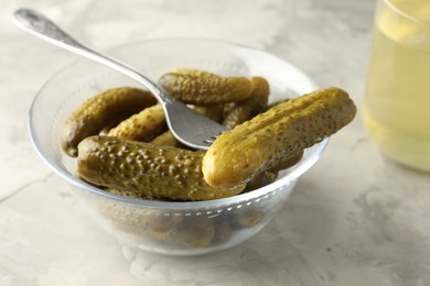 Photo of Pickled cucumbers in bowl and fork on grey textured table, closeup