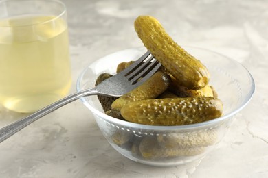 Photo of Pickled cucumbers in bowl, fork and brine on grey textured table, closeup