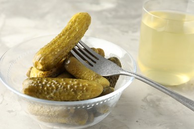 Pickled cucumbers in bowl, fork and brine on grey textured table, closeup