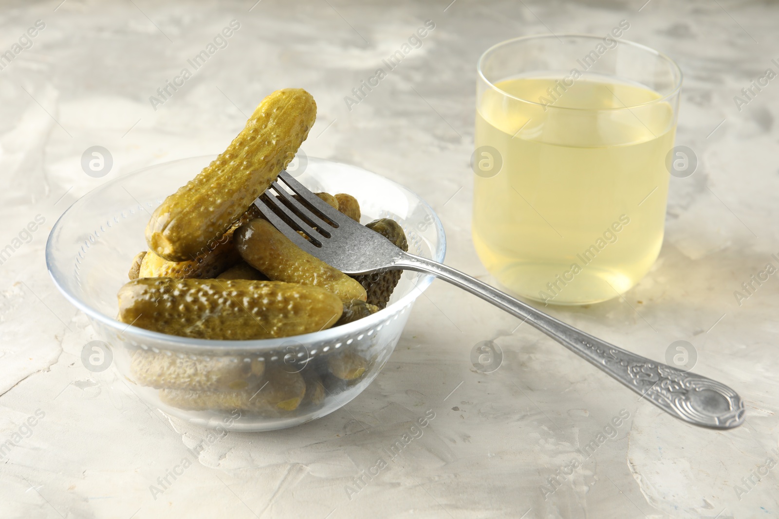 Photo of Pickled cucumbers in bowl, fork and brine on grey textured table