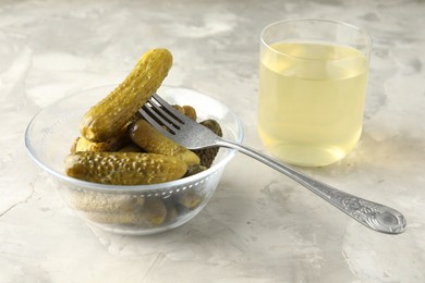 Photo of Pickled cucumbers in bowl, fork and brine on grey textured table