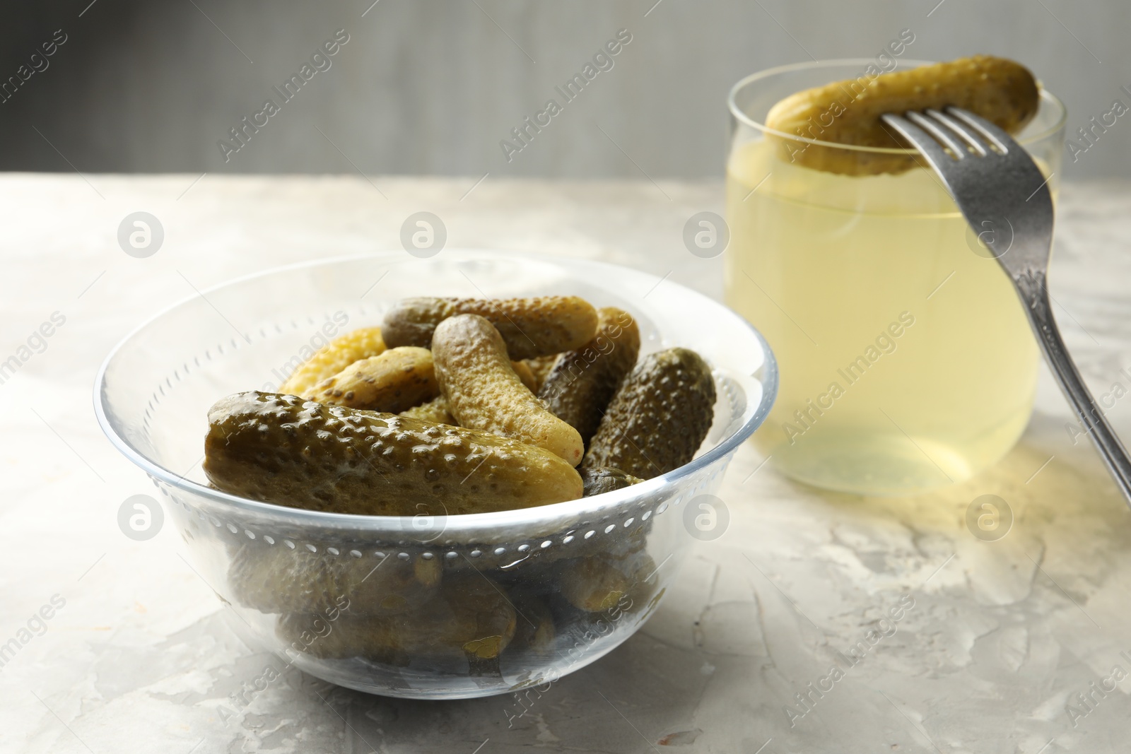Photo of Pickled cucumbers in bowl, fork and brine on grey textured table, closeup