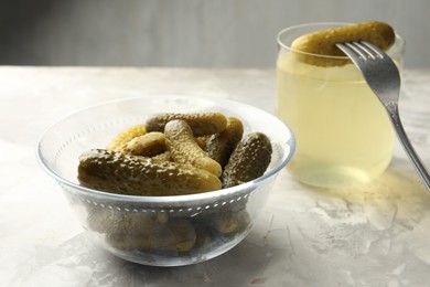 Pickled cucumbers in bowl, fork and brine on grey textured table, closeup
