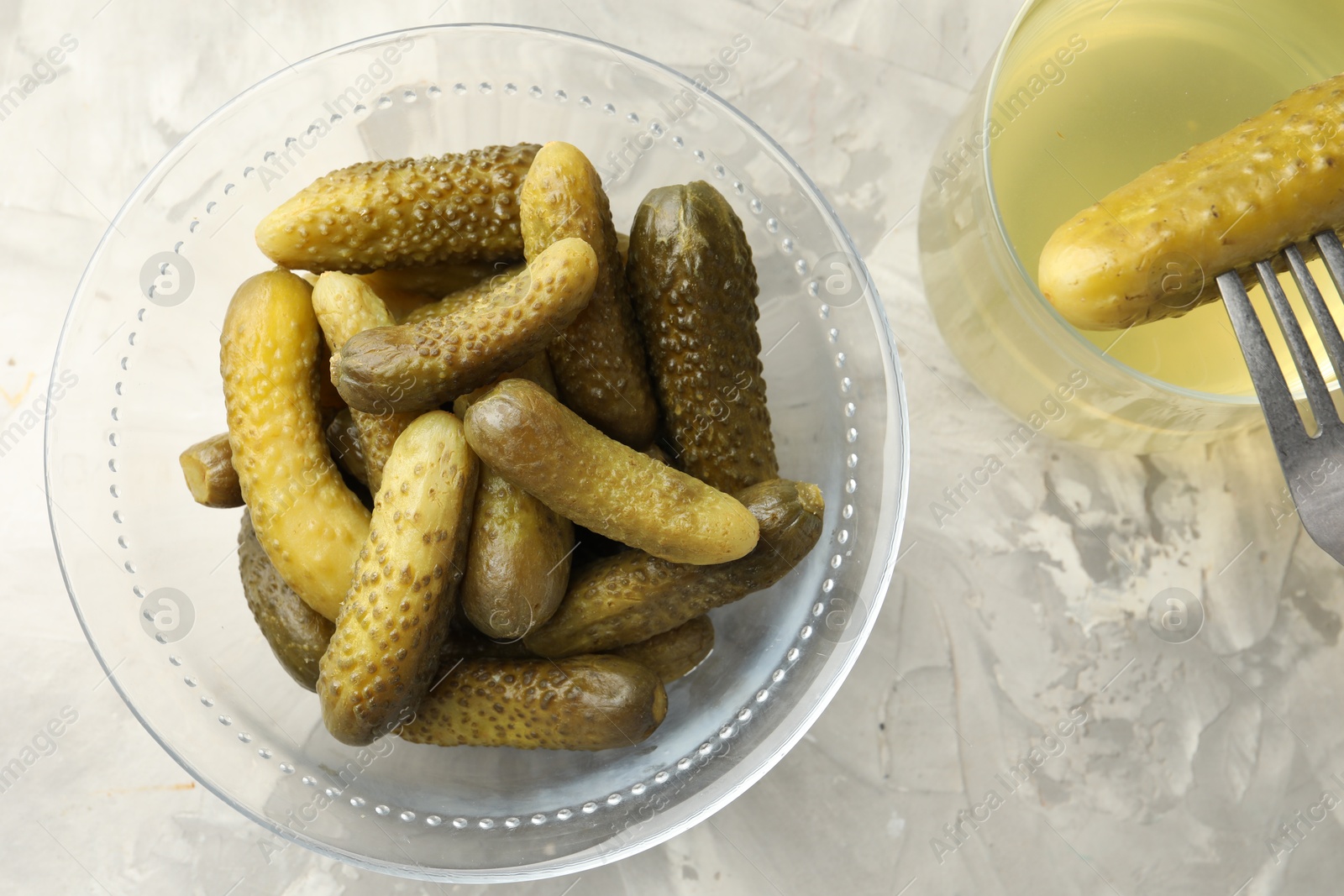 Photo of Pickled cucumbers in bowl, fork and brine on grey textured table, flat lay