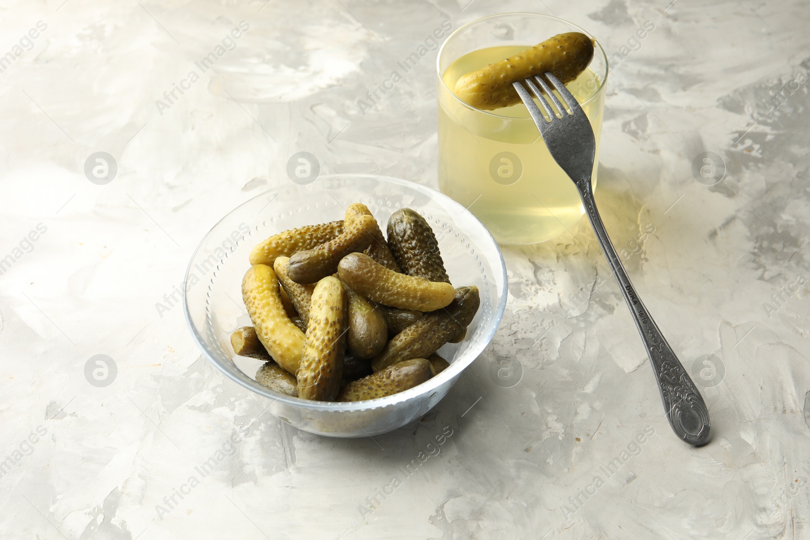 Photo of Pickled cucumbers in bowl, fork and brine on grey textured table