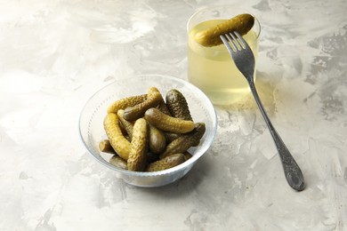 Pickled cucumbers in bowl, fork and brine on grey textured table