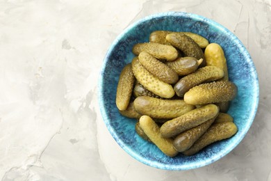 Pickled cucumbers in bowl on grey textured table, top view. Space for text