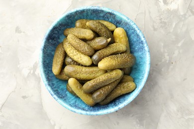 Pickled cucumbers in bowl on grey textured table, top view